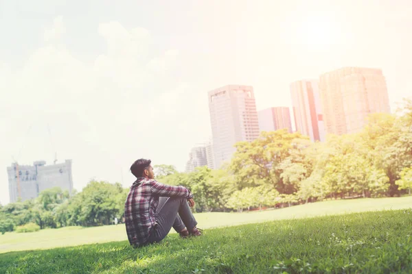 Jonge hipster man zit op gras in het park alleen tegen de — Stockfoto