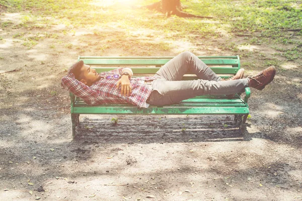 Junger Hipster legt sich auf grüne Parkbank und schaut weg. — Stockfoto