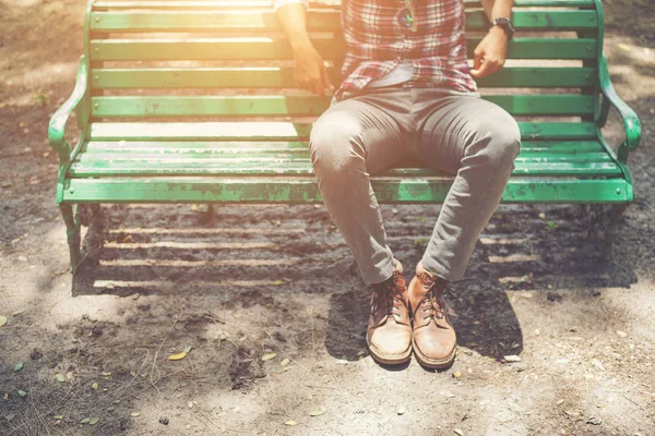 Хипстер, сидящий на скамейке в джинсах и коричневой обуви серны — стоковое фото