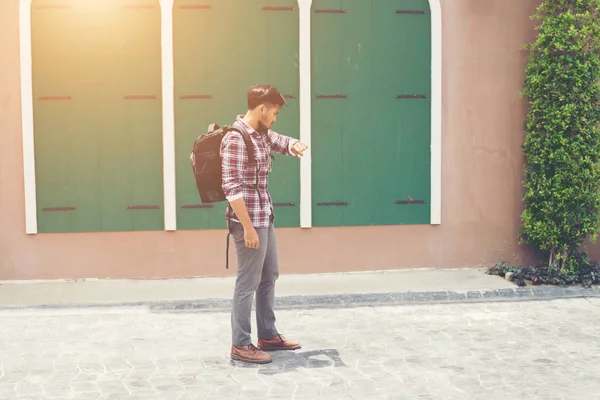 Young man looking at his hand-watch before go to travel with bac