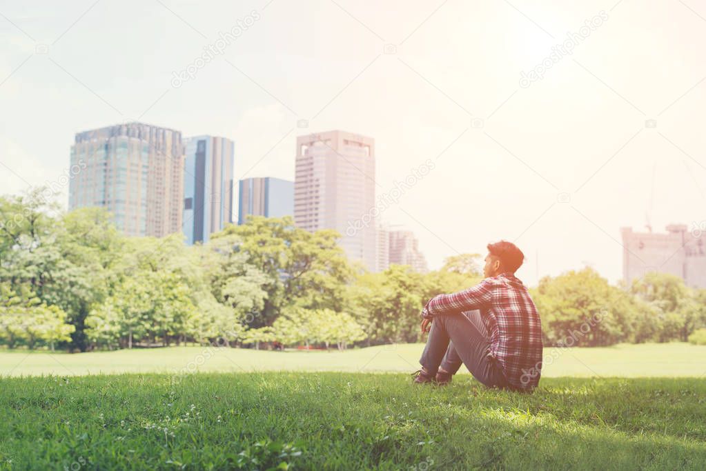 Young hipster man sitting on grass in the park alone against the