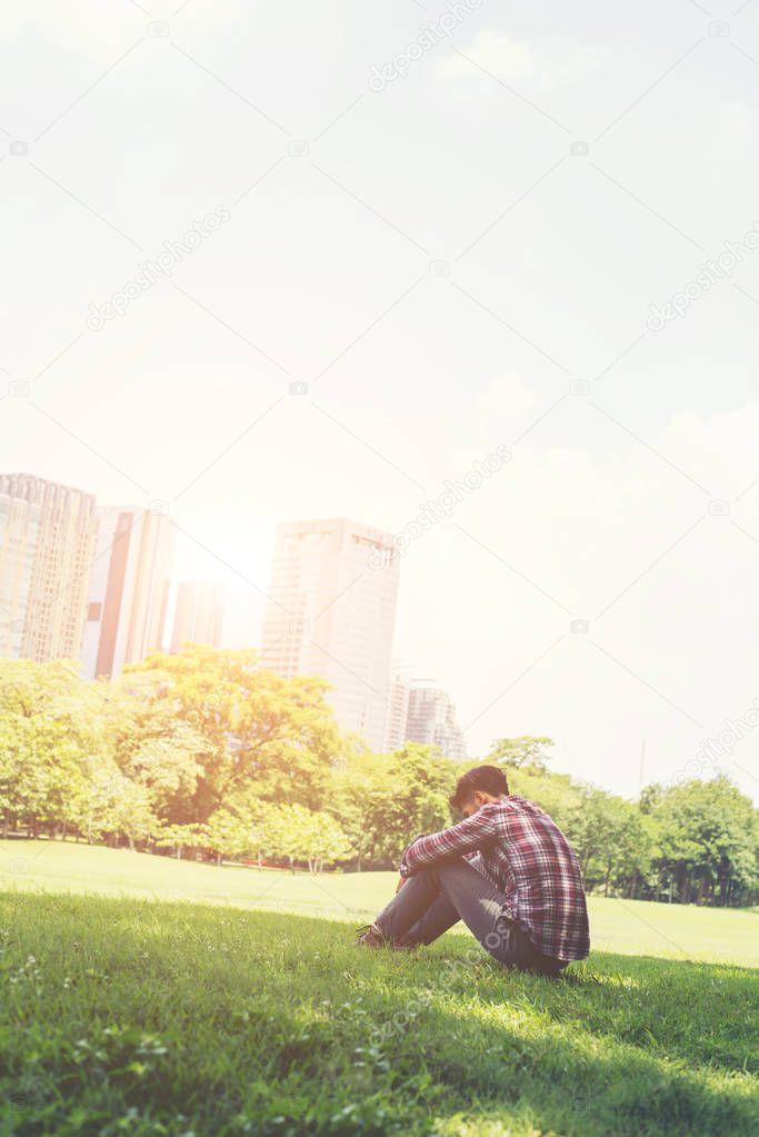 Young hipster man sitting on grass in the park alone against the