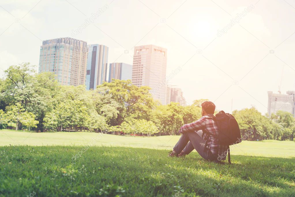 Rear view of relaxed young traveling man sitting on grass in the