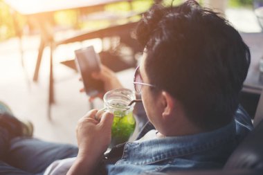 Café'de rahatlatıcı gülümseyen smartphone ile genç adam.