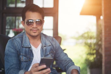 Café'de rahatlatıcı gülümseyen smartphone ile genç adam.