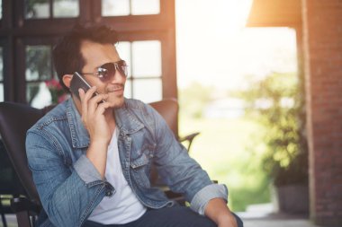 Café'de rahatlatıcı gülümseyen smartphone ile genç adam.