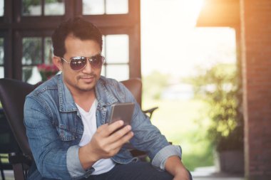 Café'de rahatlatıcı gülümseyen smartphone ile genç adam.