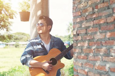 Yakışıklı adam guit oynarken bir tuğla duvara yaslanmış