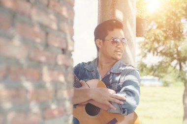 Yakışıklı adam guit oynarken bir tuğla duvara yaslanmış