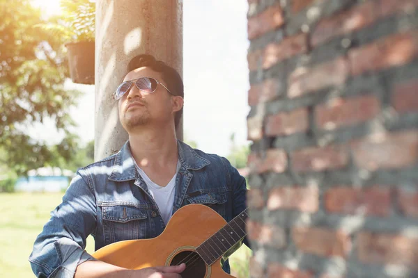 Handsome man leaning against a brick wall while playing the guit — Stock Photo, Image