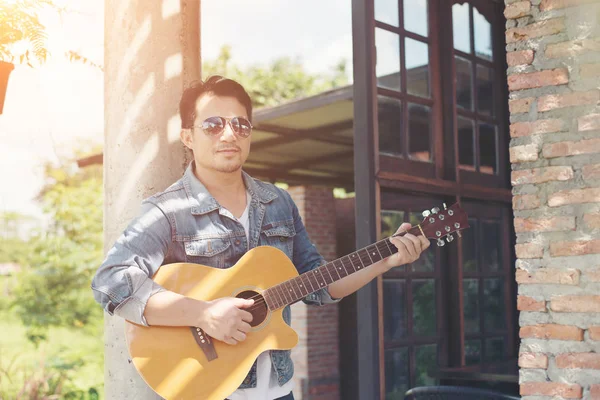 Handsome man leaning against a brick wall while playing the guit — Stock Photo, Image