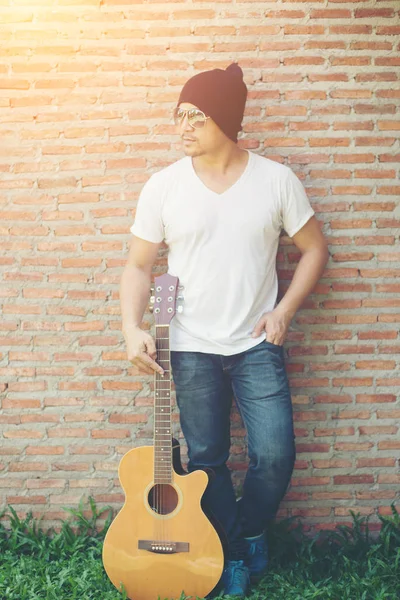 Handsome guy standing holding guitar against the brick wall posi — Stock Photo, Image