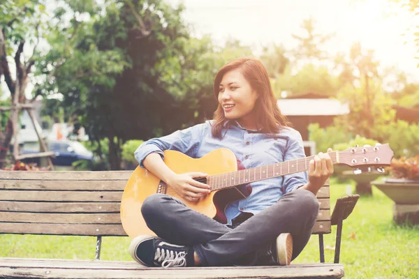 Güzel genç kadın mutlu tim banktaoturuyor, gitar çalmak