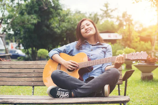Beautiful young woman playing guitar sitting on bench, Happy tim — Stock Photo, Image