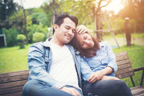 Young smiling couple looking on each other while sitting on benc — Stock Photo, Image