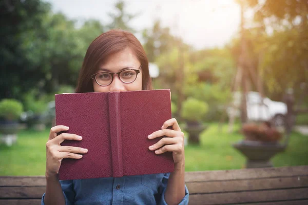 Joven chica hipster sonriendo y cubierto la cara por su libro rojo whil — Foto de Stock