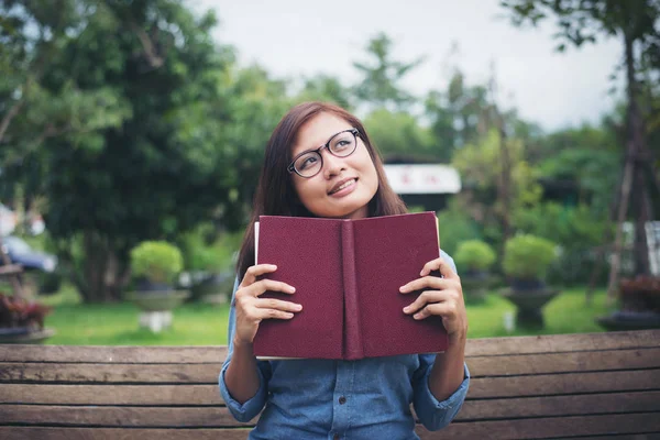 Hipster menina encantadora pensando em algo ao ler livro vermelho — Fotografia de Stock