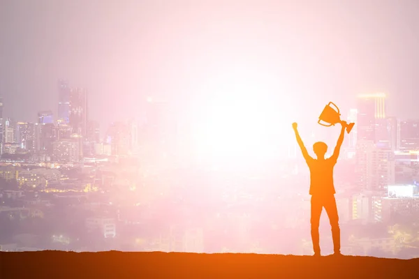 Silhouette man holding up a gold trophy cup as a winner in a com