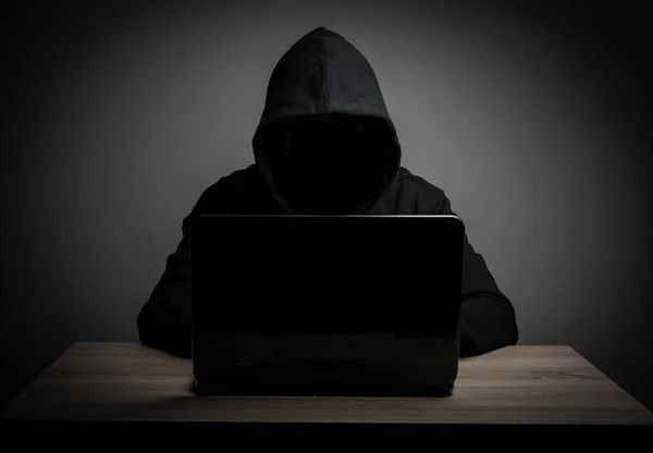 Hacker trabajar frente a su ordenador portátil con la cara oscura . — Foto de Stock