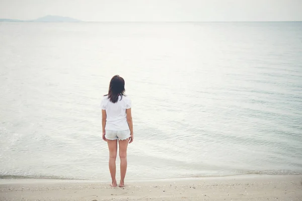 Traseira da jovem mulher de pé na praia com os pés descalços . — Fotografia de Stock