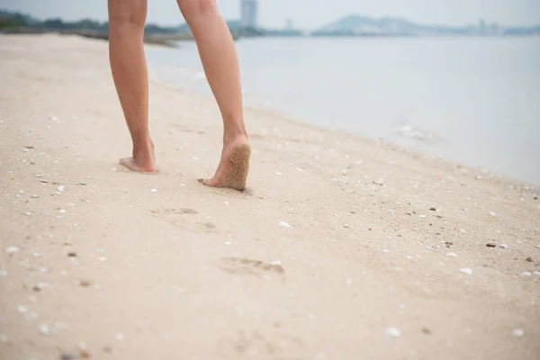 Ung kvinna promenader på sandstrand lämnar fotspår i sanden — Stockfoto