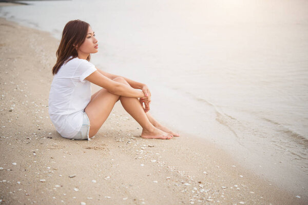 Young woman with looks lonely feel sit on the beach. Looking awa