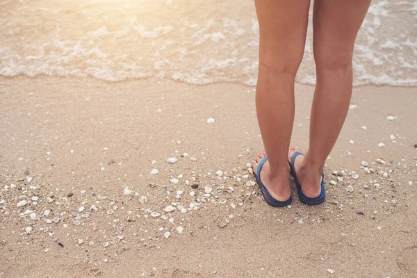 Stock image Young woman legs in flipflop sandals on sea beach.