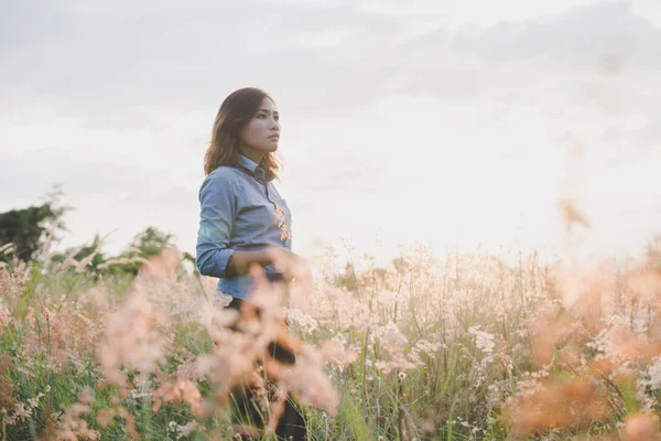 Woman looking away, standing in field with sunset background.