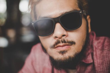 Bir barda oturan genç hipster adam giyen güneş gözlüğü c masa