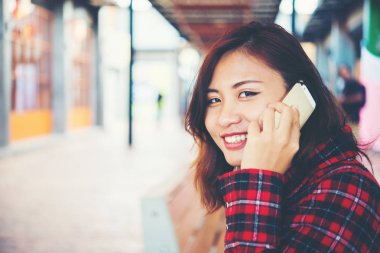 Güzel genç yenilikçi bir bankta oturan smartphone cep telefonu ile konuşmak