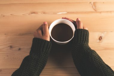 Kahve ahşap sekmesinde tutan kazaklı kadının eller