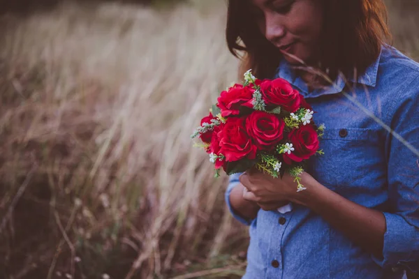 Young hipster woman in field holding a bouquet of red rose, summ
