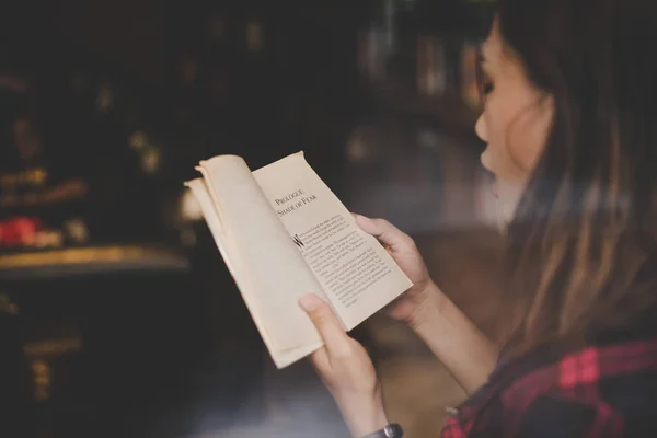 Ung charmig kvinna läser bok sittande inomhus i café. Casual — Stockfoto