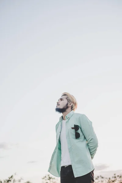 Jeune homme hipster debout dans le parc avec le ciel regardant loin . — Photo