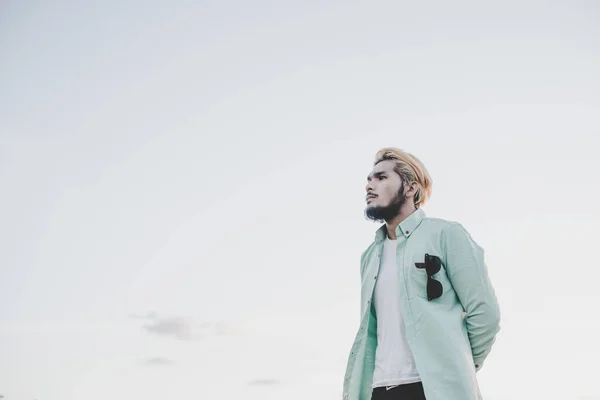 Jeune homme hipster debout dans le parc avec le ciel regardant loin . — Photo