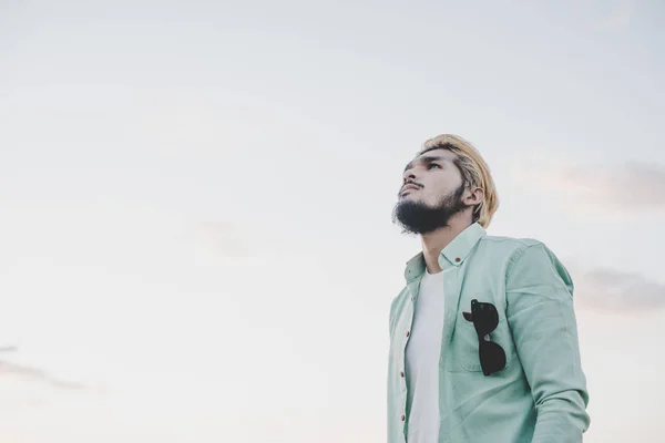 Unga hipster mannen står i parken med himlen tittar bort. — Stockfoto