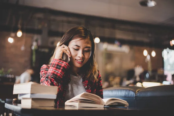 Unga hipster kvinna pratar telefonen medan du läser en bok på caf — Stockfoto