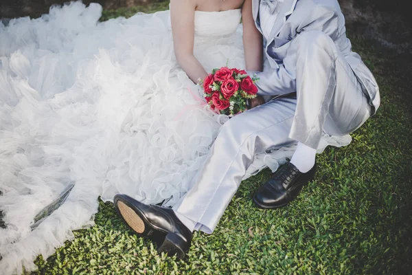 Noiva mantém um buquê de rosa vermelha de casamento em mãos, os abraços do noivo — Fotografia de Stock