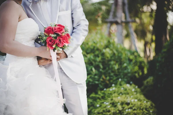 Bruid houdt een bruiloft rode roos boeket in handen, de bruidegom hugs — Stockfoto