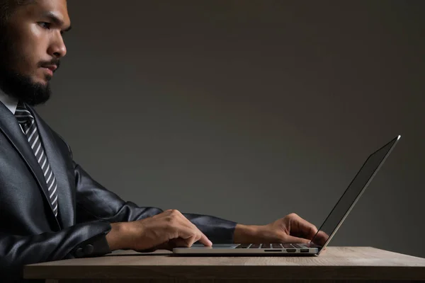Young businessman sitting working with laptop isolated on black. — Stock Photo, Image