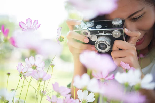 Hipster girl with vintage camera focus shooting flowers at garde