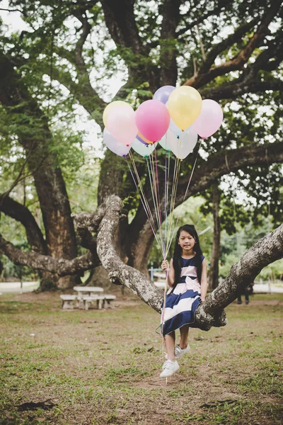 Piccolo carino asiatico ragazza seduta su albero ramo con colorful di b — Foto Stock