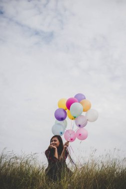 Holding renkli balonlar alanında, mavi gökyüzü arka planda oturan genç hipster kadın.