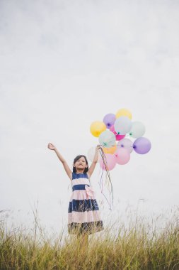 Balonlarla meadows sahada oynayan küçük kız.