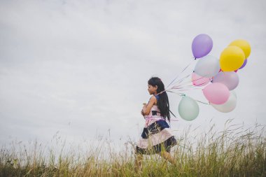 Balonlarla meadows sahada oynayan küçük kız.