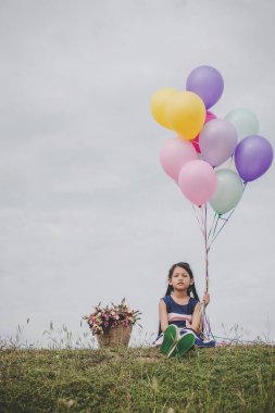 Küçük şirin kız dışında uzun yeşil çimenlerin üzerinde oturuyor. Renkli balonlar elinde tutan kız. 