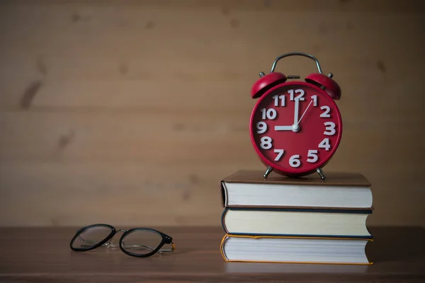 木製テーブルの上のグラスと書籍のスタックに で目覚まし時計 教育コンセプト — ストック写真