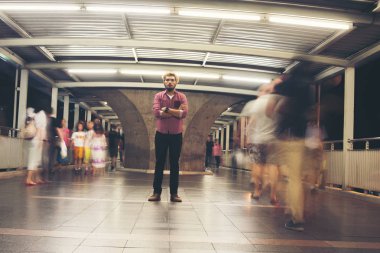 Hipster sakallı adam geceleri seyahat ederken insanlar hareketli arka plan ile katta ayakta.