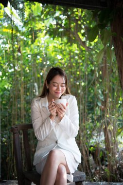 Uzakta mutlu gülümseme, iyi bir hava için memnun ile seyir, işe gitmeden önce kahve ile rahatlatıcı bir genç kadın.