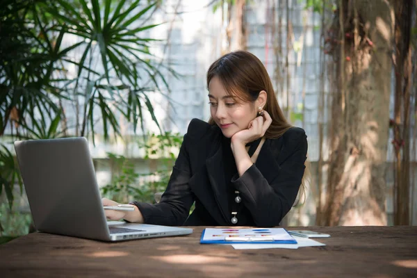 Executive thinking over working schedule for employee writing report into notebook while using laptop computer.